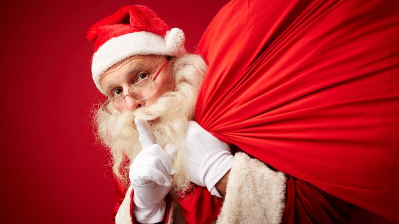 Santa with sack of Christmas gifts asking for silence.