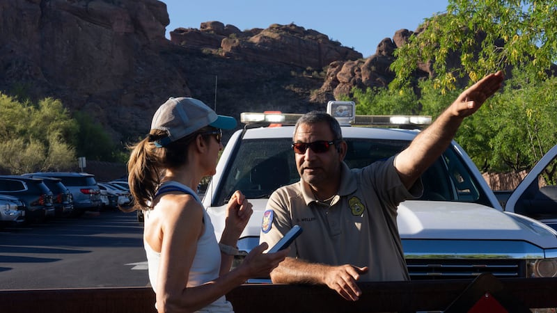 Un guardaparques le da instrucciones a una excursionista debido al calor extremo en Camelback...